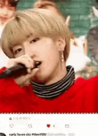 a young man is singing into a microphone while wearing a red sweater and striped turtleneck .