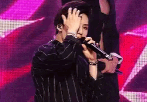 a man is singing into a microphone and covering his face .