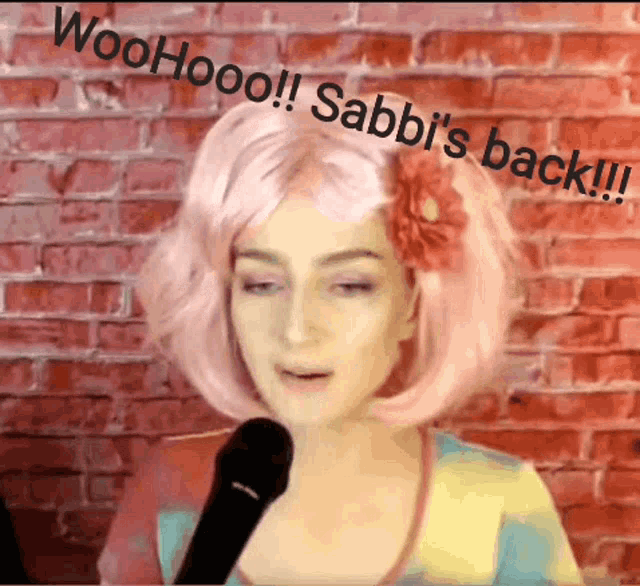 a woman in a pink wig is talking into a microphone and says woohoo !!! sabbi 's back