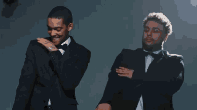 a man in a tuxedo stands next to another man in a tuxedo