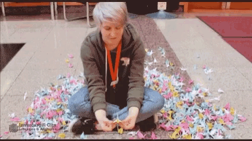 a woman is sitting on the floor with a bunch of origami flowers around her