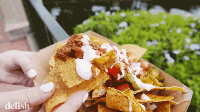a close up of a person holding a tray of nachos with the word delish on the bottom