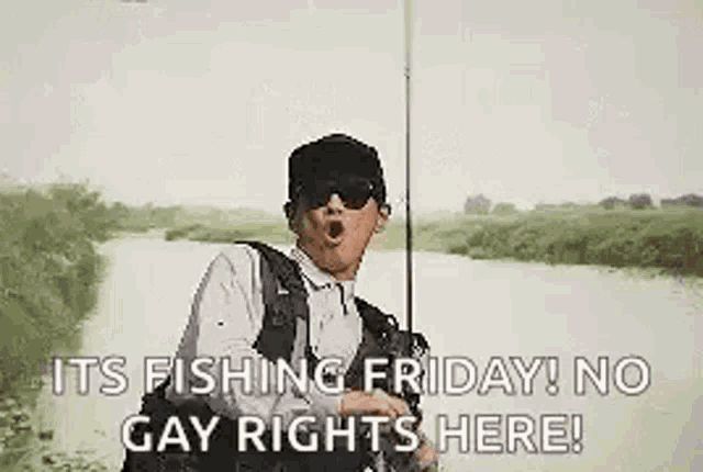 a man is holding a fishing rod and a fish in his hand while standing next to a river .
