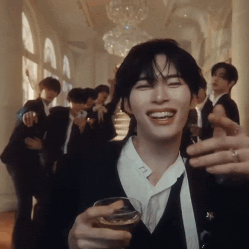 a man in a suit is holding a glass of wine and smiling in front of a group of men .