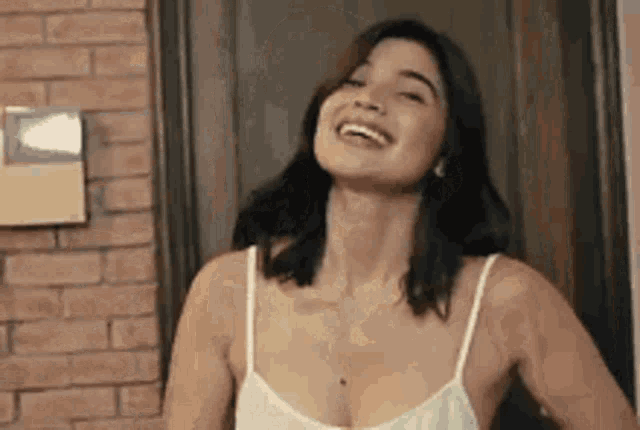 a woman in a white tank top is laughing with her eyes closed .