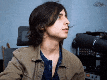 a man with long hair is sitting in front of a microphone with the letters a and g on the bottom