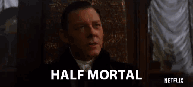a man in a suit and tie is sitting in a chair with the words half mortal written on the bottom .