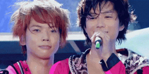 two young men are standing next to each other on a stage . one of the men is singing into a microphone .