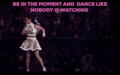 a woman in a neon outfit is dancing in front of a crowd of people with their hands in the air .