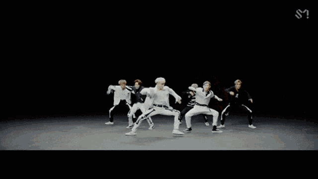 a group of young men are dancing in a room with the letter s on the bottom right