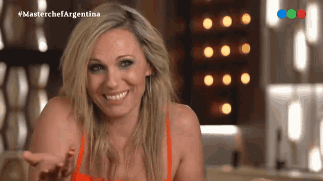 a blonde woman is smiling in front of a screen that says #masterchefargentina