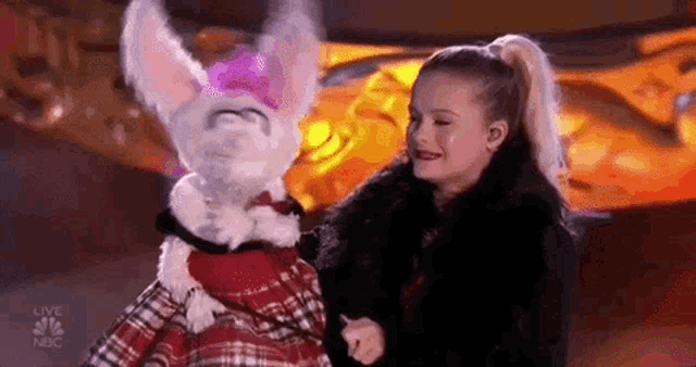 a little girl is standing next to a stuffed bunny rabbit .