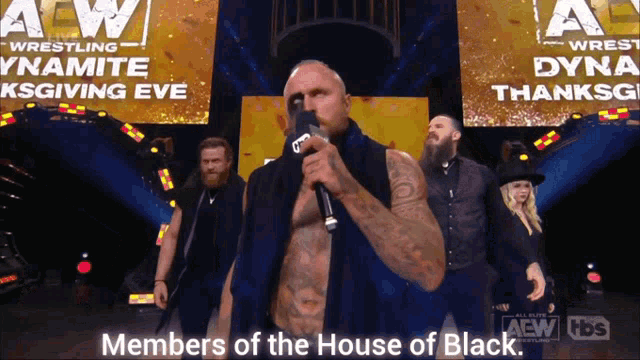a man stands on a stage holding a microphone with the words members of the house of black behind him