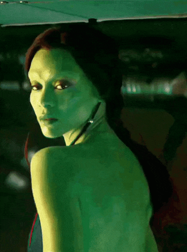 a woman with green skin is looking over her shoulder at the camera
