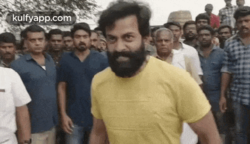a man with a beard is standing in front of a crowd of people wearing a yellow t-shirt .