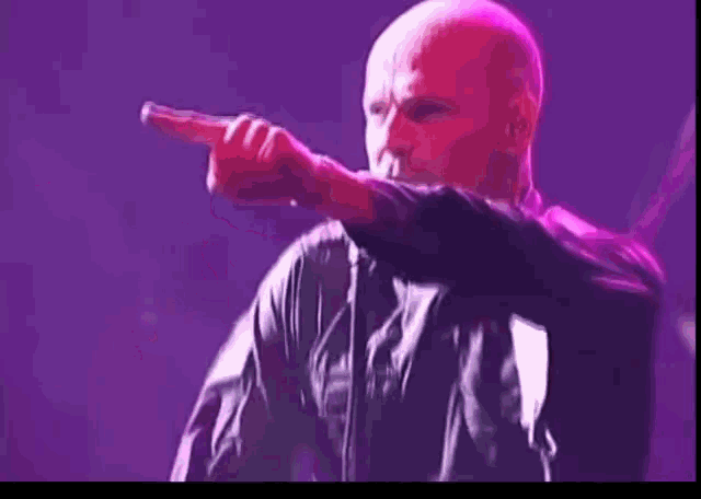 a bald man is singing into a microphone on a stage