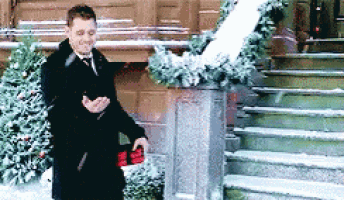a man in a suit and tie is standing in front of a staircase in the snow holding a red box .