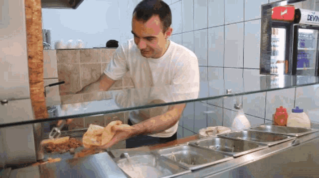 a man in a white shirt is preparing food in front of a fridge that says ' coca cola '