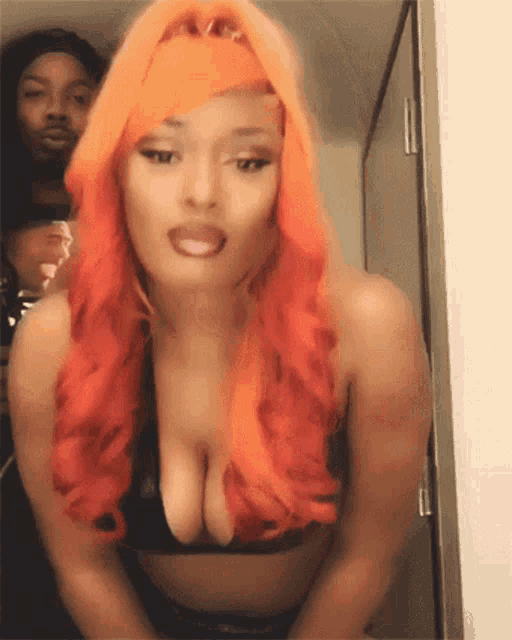 a woman with orange hair and a black bra is standing in front of a man