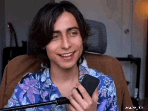 a young man is sitting in a chair holding a cell phone in his hand and smiling .
