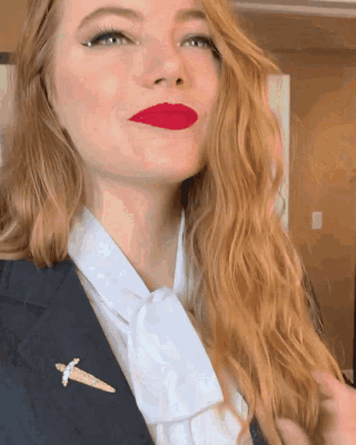 a woman wearing red lipstick and a suit has a brooch on her jacket