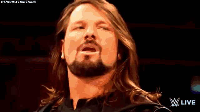 a wrestler with long hair and a beard is standing in a ring with his mouth open .