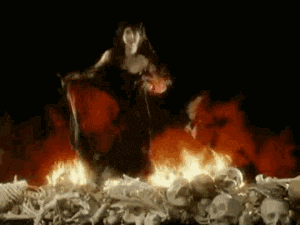 a woman in a black dress is standing in a pile of skulls and bones in front of a fire .