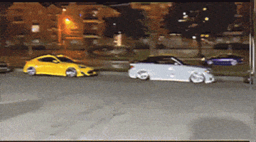 a yellow car and a white car are driving down a street at night
