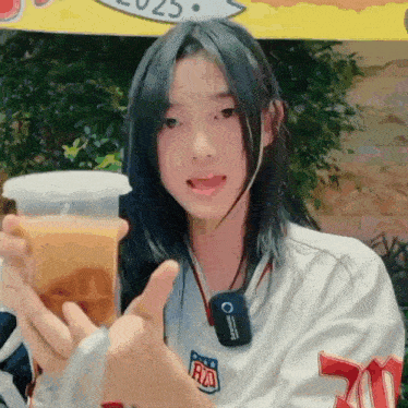 a girl is holding a cup of orange juice and giving a thumbs up