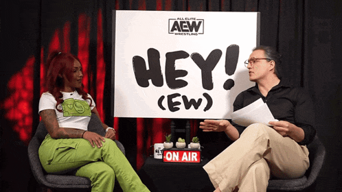 two people are sitting in front of a sign that says hey ( ew )