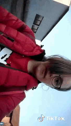 a girl wearing glasses and a red jacket has tik tok written on her face