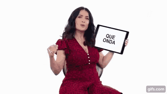 a woman in a red dress is sitting in a chair holding a tablet with the words `` que onda '' on it .