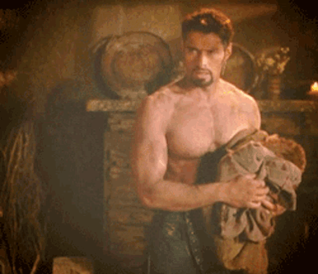 a shirtless man with a beard is standing in front of a fireplace