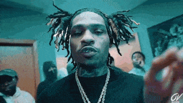a man with dreadlocks is wearing a black shirt and a chain around his neck