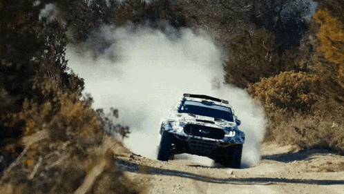 a ford truck is driving down a dirt road with smoke coming out of it