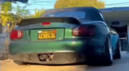a green car with a license plate that says lcm634 is driving down the street .
