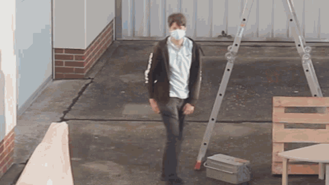 a man wearing a face mask is standing in front of a ladder