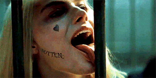 a woman with a tattoo on her face is sticking her tongue out behind a fence .