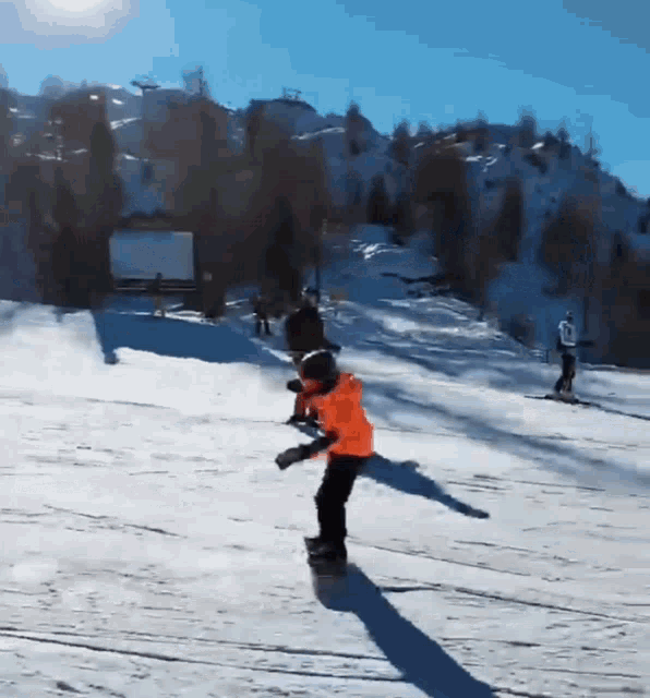 a little boy in an orange jacket is skiing down a snowy slope