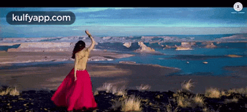 a woman in a red dress is standing on top of a hill with her arms outstretched .