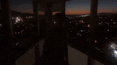 a woman in a white dress is standing in front of a large window overlooking a city