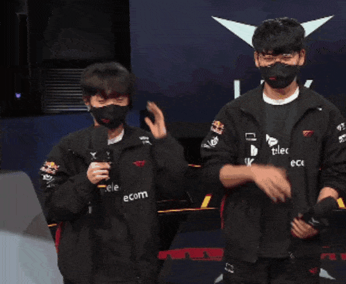 a man wearing a mask stands next to another man wearing a black shirt with the letter k on it