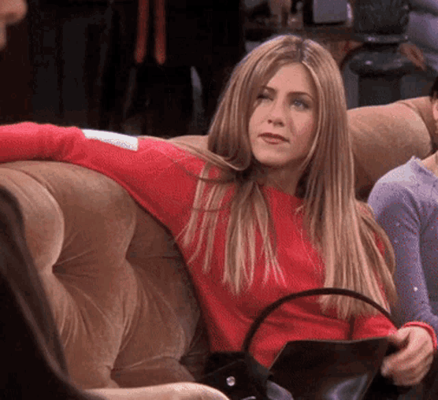 a woman is sitting on a couch wearing a red sweater