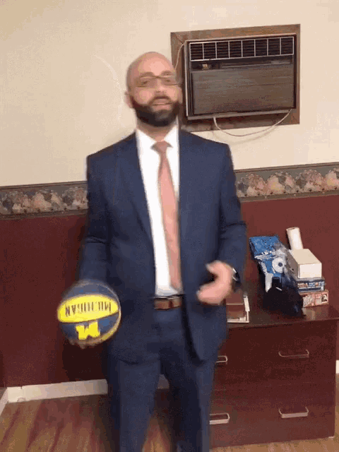a man in a suit and tie holds a michigan basketball