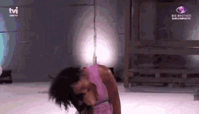a woman in a pink dress is hanging upside down on a rope in a room .