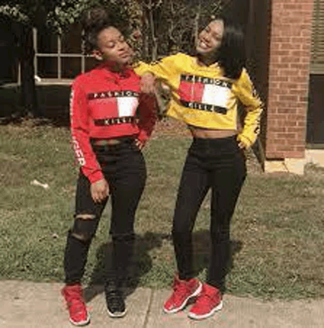 two girls are standing next to each other on a sidewalk wearing tommy hilfiger shirts .