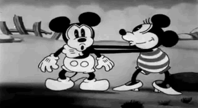 a black and white cartoon of mickey mouse and minnie mouse standing next to each other on a beach .