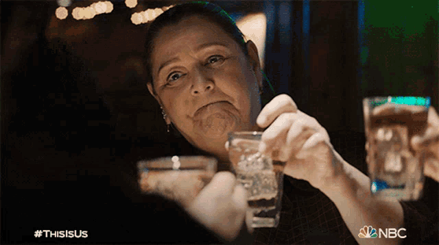 a woman is holding two shot glasses with nbc written on the bottom right
