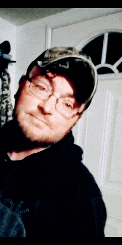 a man wearing glasses and a hat stands in front of a white door