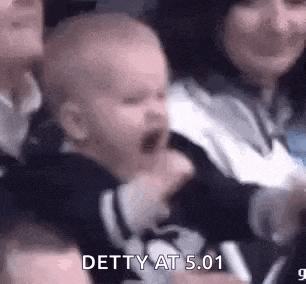 a baby is screaming in a crowd of people while sitting in a stadium .